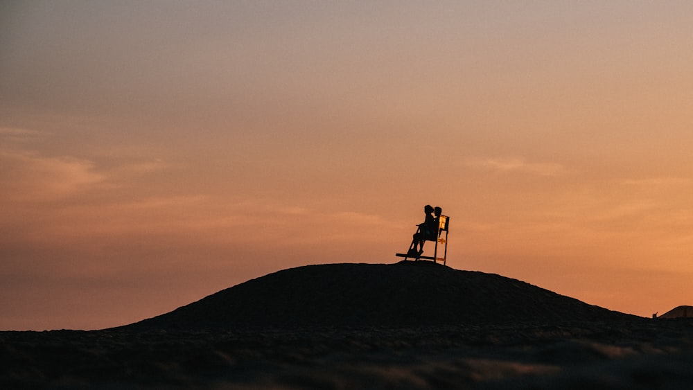 Silhouette von 2 Personen, die während des Sonnenuntergangs auf dem Gipfel des Berges stehen