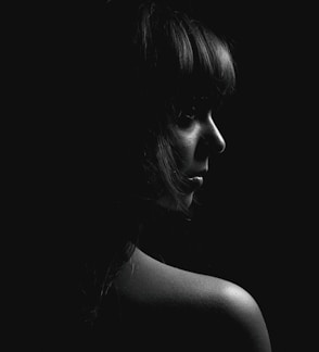 A striking black and white portrait of a woman with soft lighting highlighting her features against a charcoal grey background.
