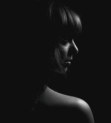 A striking black and white portrait of a woman with soft lighting highlighting her features against a charcoal grey background.