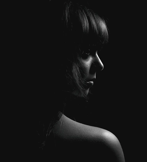A striking black-and-white portrait of a model bathed in soft, natural light against a charcoal backdrop.