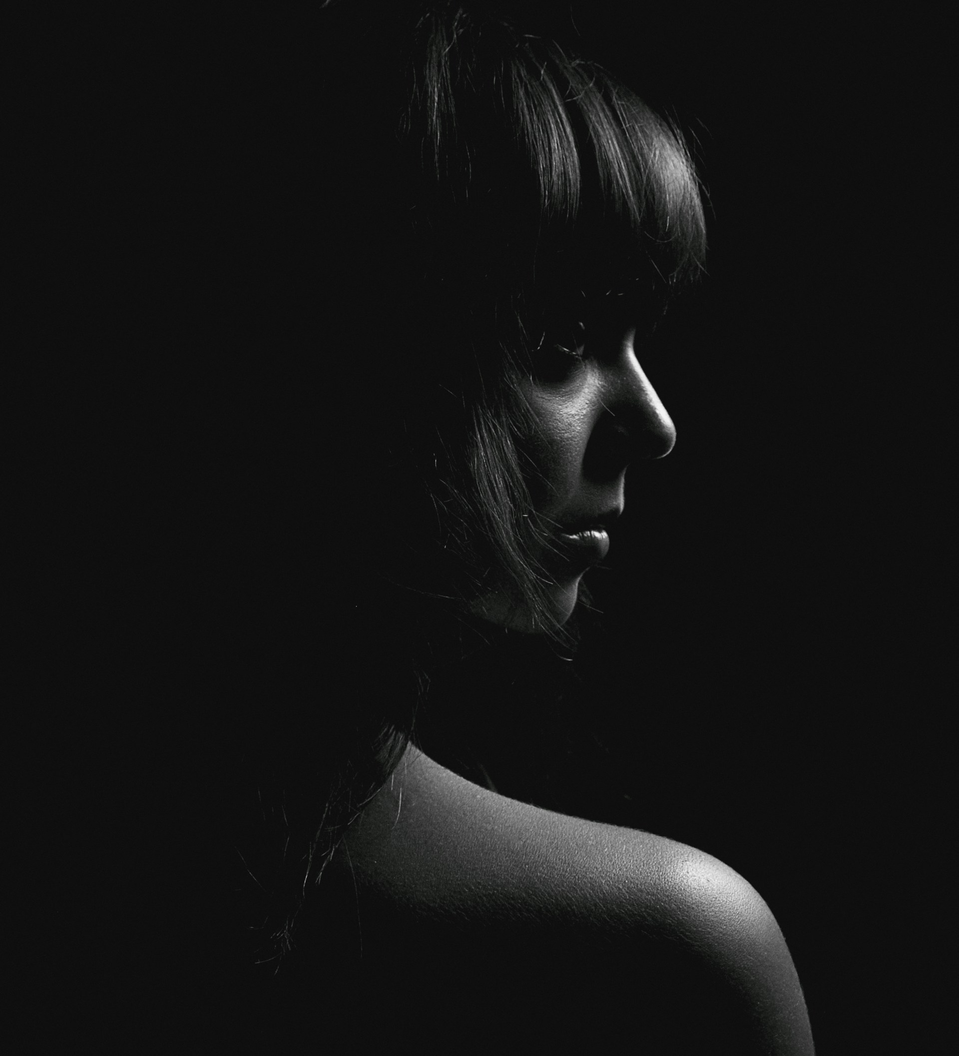 An artistic portrait of a model with soft lighting highlighting curves, set on a minimalist black background.