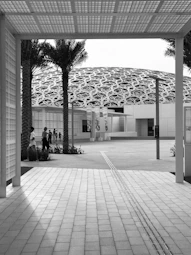 grayscale photo of people sitting on bench near building