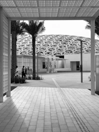 grayscale photo of people sitting on bench near building