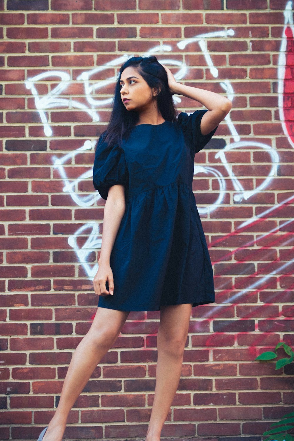 Femme en robe bleue debout sur un mur de briques brunes