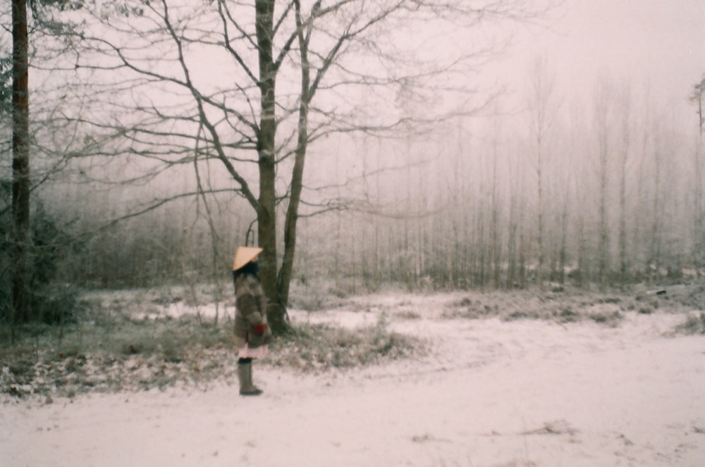 woman in black jacket and brown hat standing under brown tree during daytime