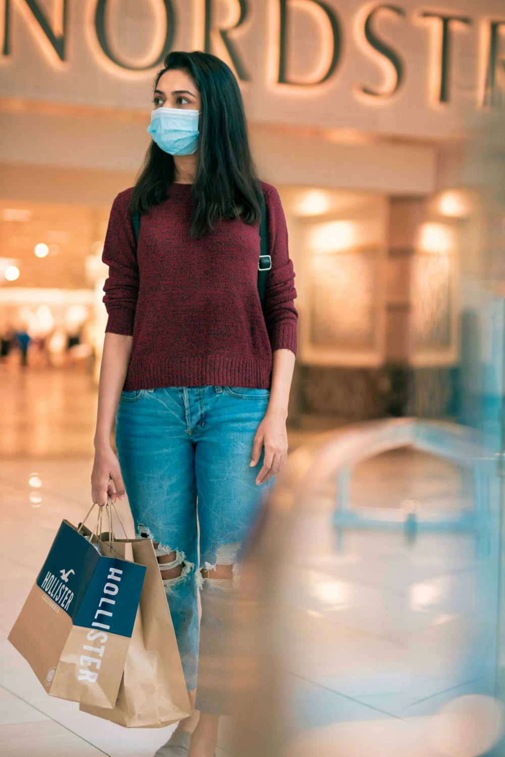 Mujer con camisa roja de manga larga y jeans de mezclilla azules sosteniendo una bolsa de compras azul