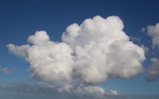 A large, fluffy cloud formation fills the sky with a deep blue background, while smaller cloud patches surround it. The clouds are bright white with soft, billowy textures.