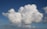 A large, fluffy cloud formation fills the sky with a deep blue background, while smaller cloud patches surround it. The clouds are bright white with soft, billowy textures.