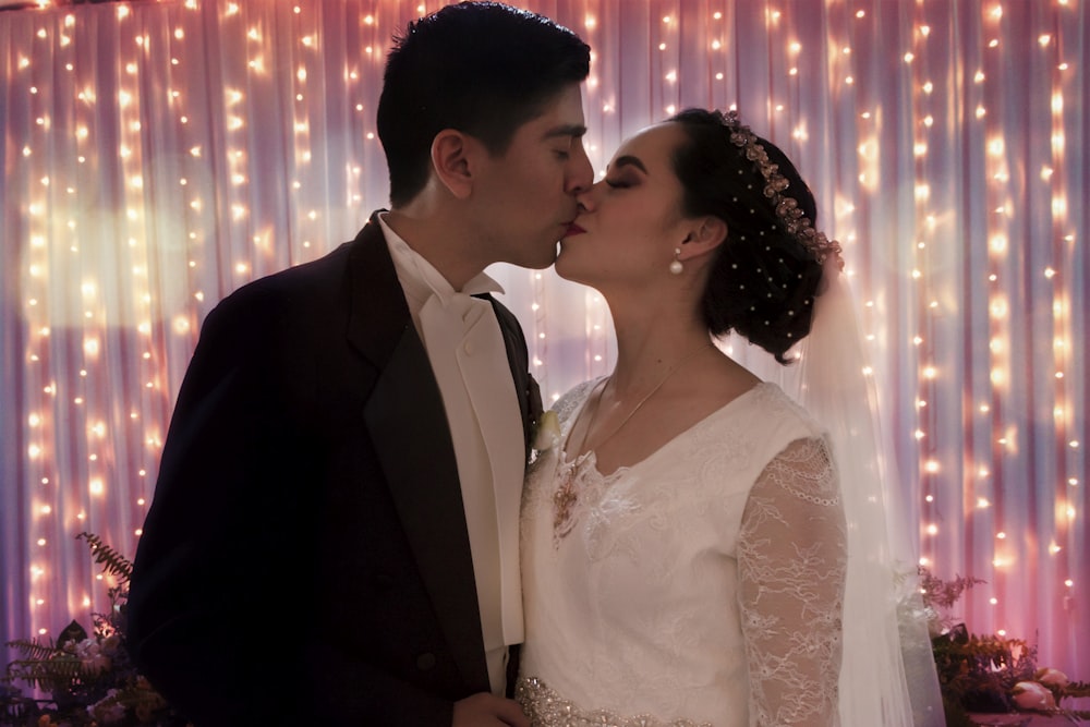 man in black suit kissing woman in white floral lace wedding dress