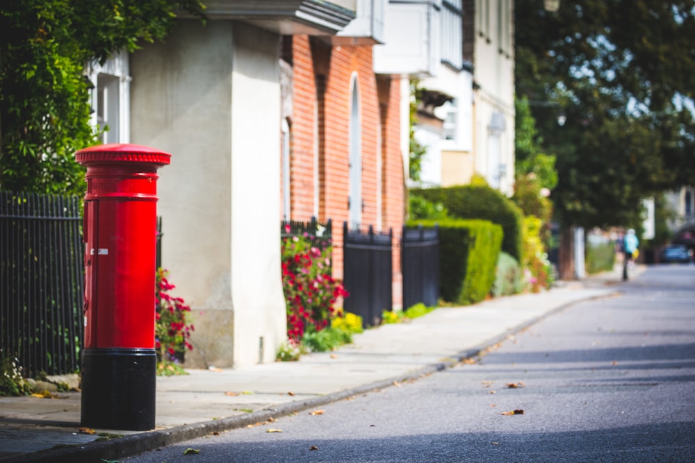 red and black trash bin on sidewalk during daytime