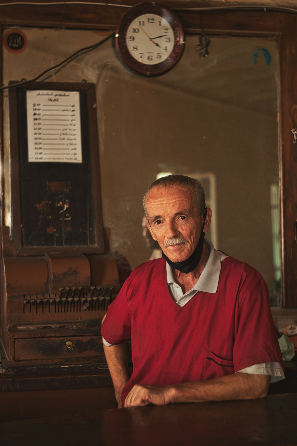 man in red polo shirt standing beside brown wooden piano