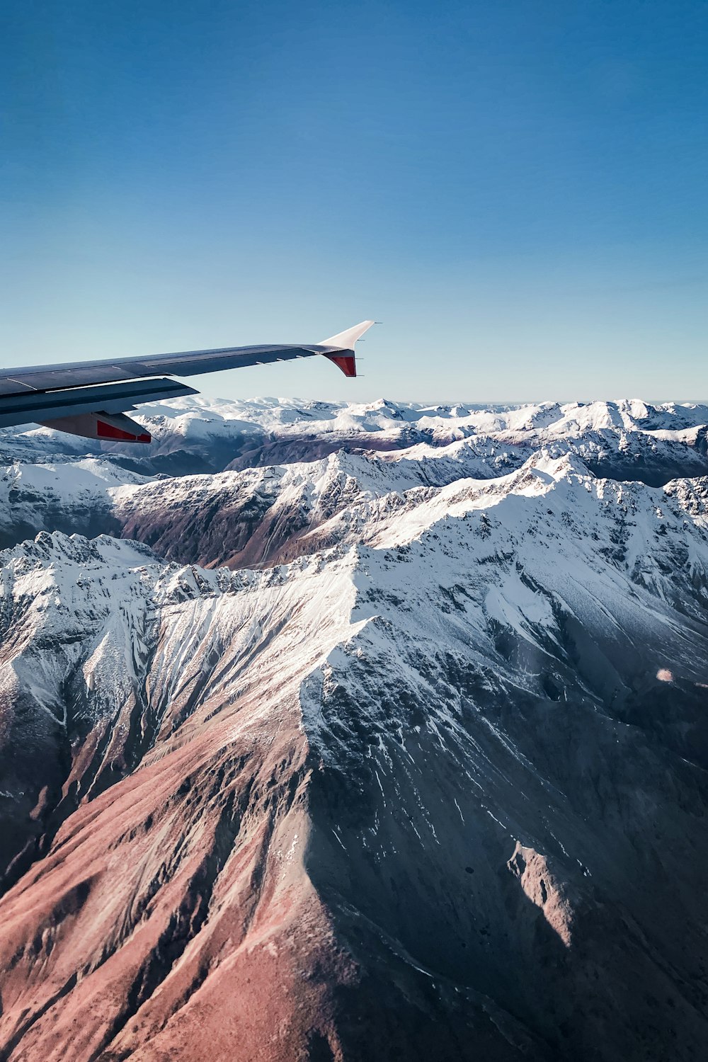 red and white airplane wing over snow covered mountain during daytime