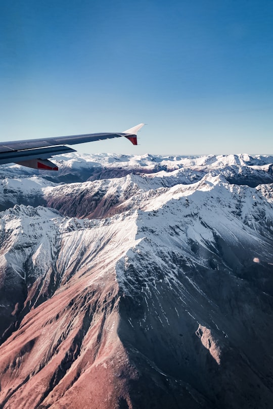 red and white airplane wing over snow covered mountain during daytime in Southern Alps New Zealand