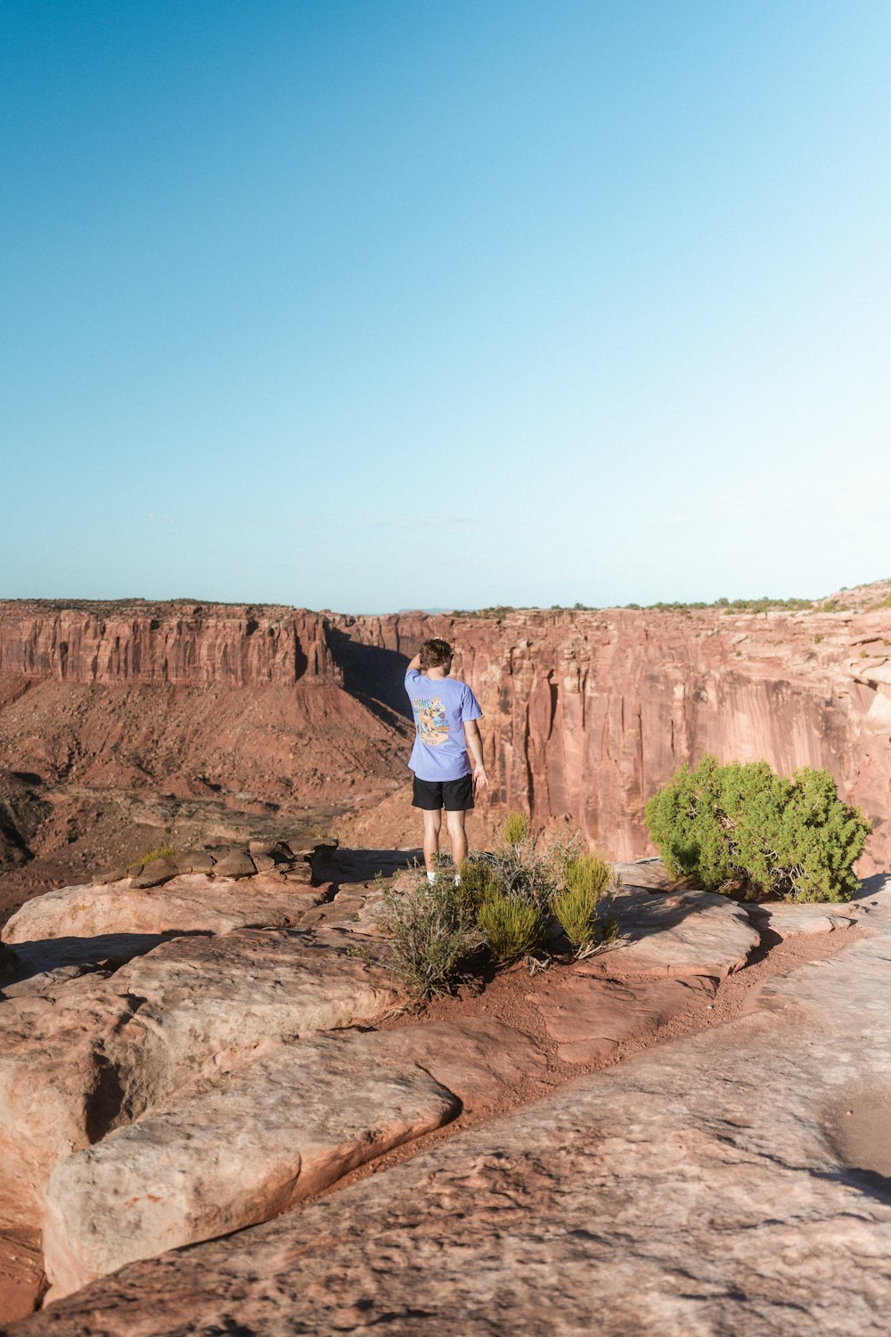 man in blue shirt standing on brown rock formation during daytime