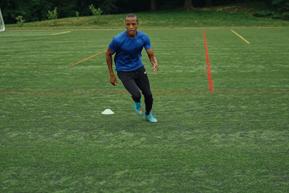 Hombre con camiseta azul Nike de cuello redondo y pantalones negros corriendo en el campo de hierba verde