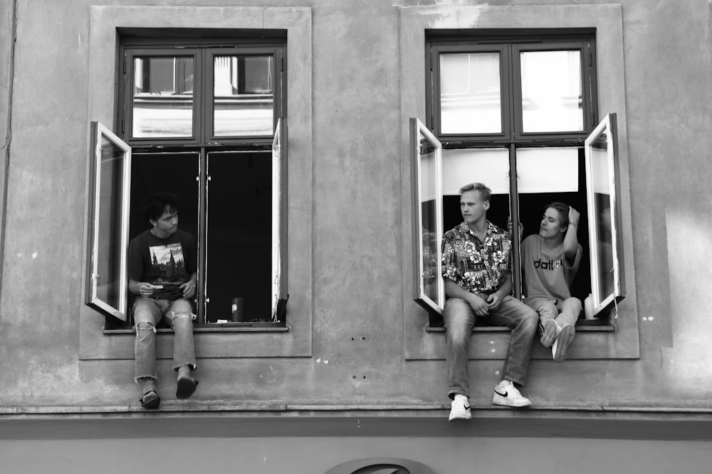 grayscale photo of 2 men and 2 women sitting on window