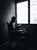 A contemplative person sitting by a window with a notebook.