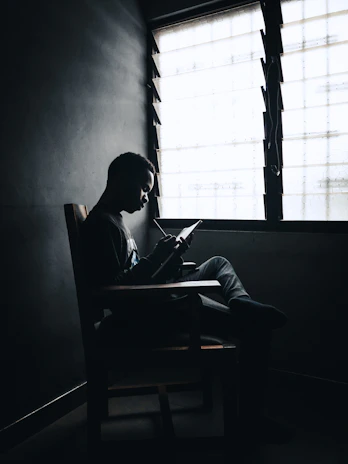 An author seated by a window, pen in hand, capturing ideas in a journal.