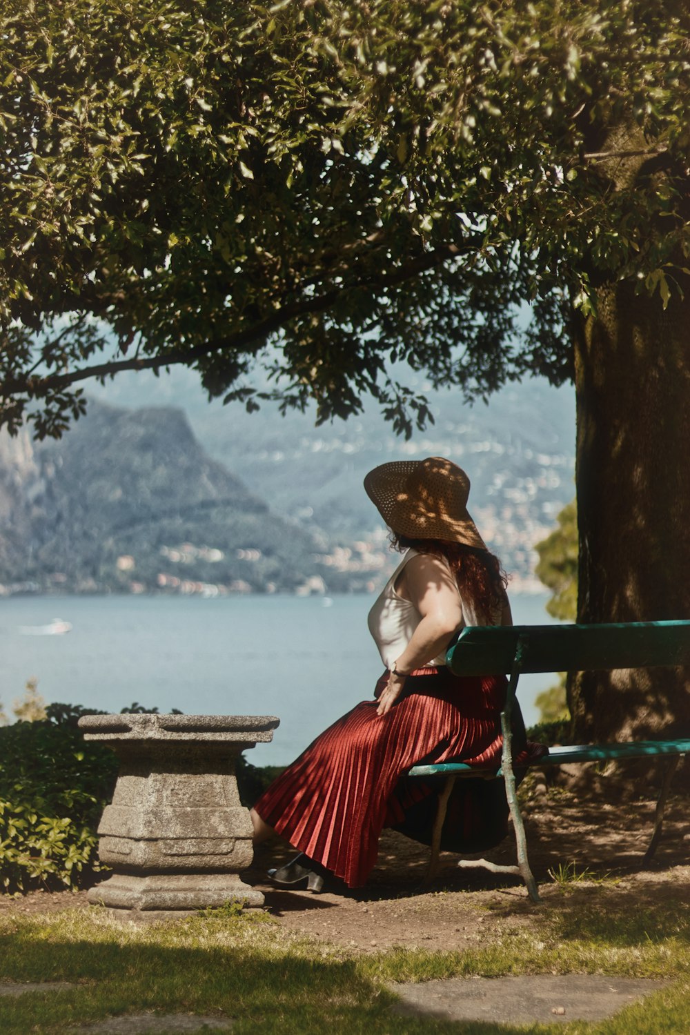 woman in red and black dress wearing brown hat sitting on brown wooden bench