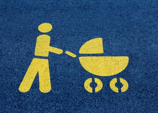 A yellow painted symbol on a dark asphalt surface depicts a person pushing a baby stroller.