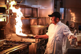 Chef preparing ayam pop in the kitchen, showcasing the cooking process with flames and fresh ingredients.