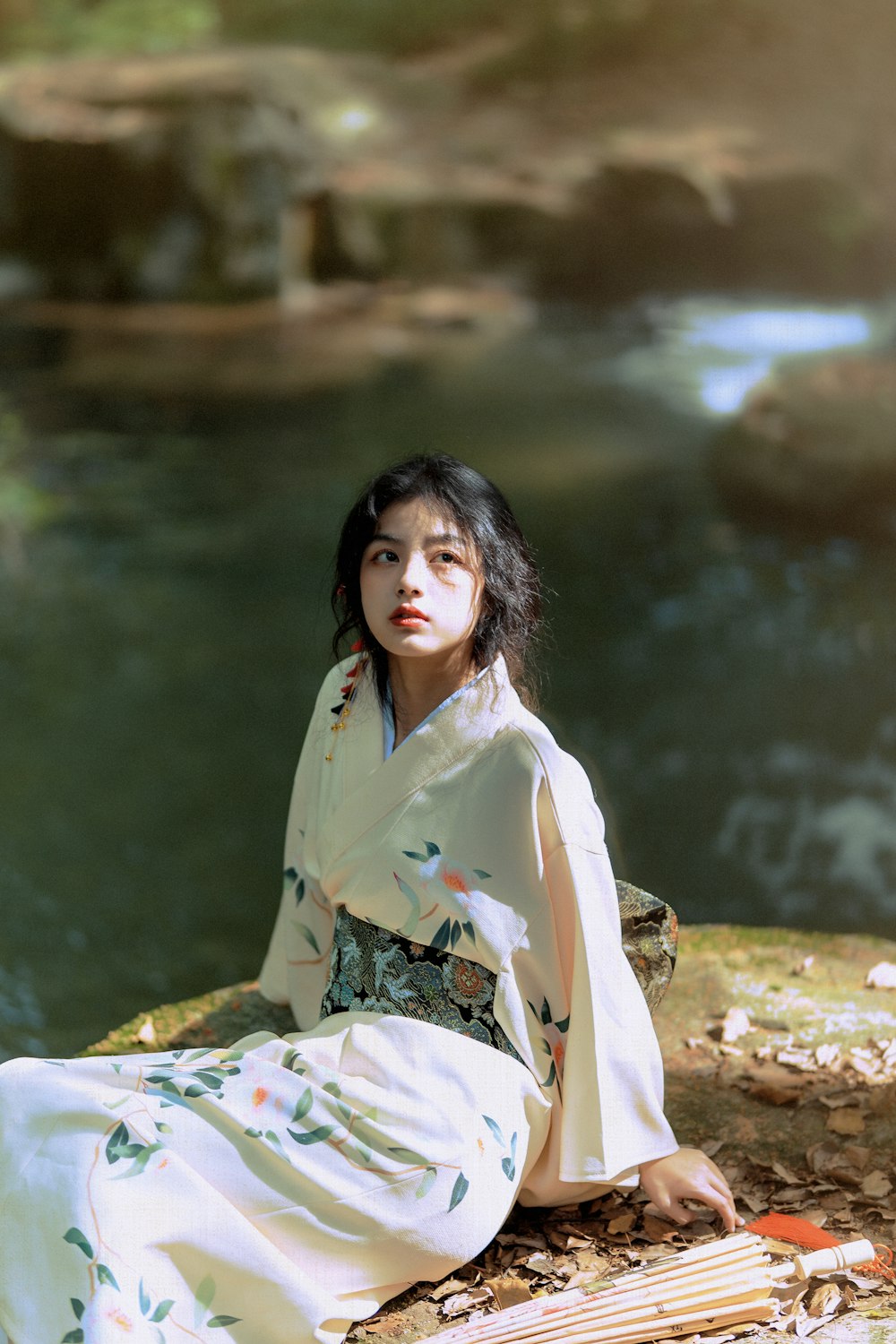 woman in green and white floral kimono sitting on rock near river during daytime