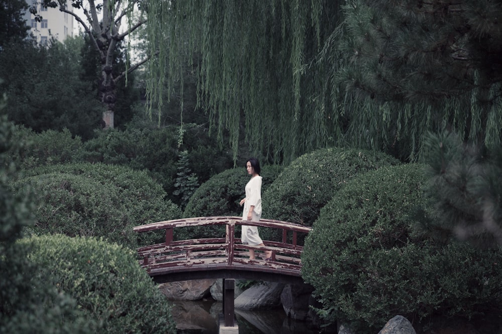 woman in white dress standing on brown wooden bridge