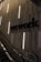A dimly lit modern interior with an escalator and a wall featuring vertical light strips. The word 'wework' is prominently displayed on the wall in bold letters. The setting appears corporate or industrial with a sleek and minimalist design.