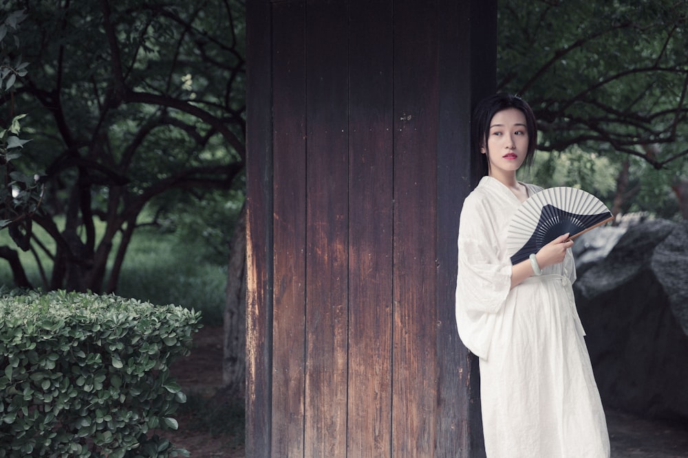 woman in white long sleeve dress standing beside brown wooden wall