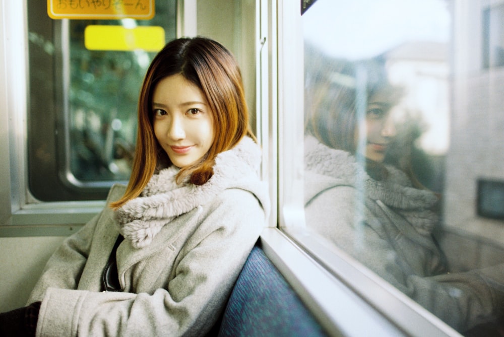 woman in white coat sitting beside glass window