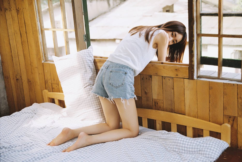 woman in white shirt and blue denim shorts lying on bed