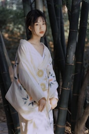 A person wearing a traditional garment stands amidst tall bamboo trees, with soft natural lighting creating a peaceful and serene atmosphere.