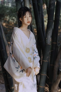 A person wearing a traditional garment stands amidst tall bamboo trees, with soft natural lighting creating a peaceful and serene atmosphere.