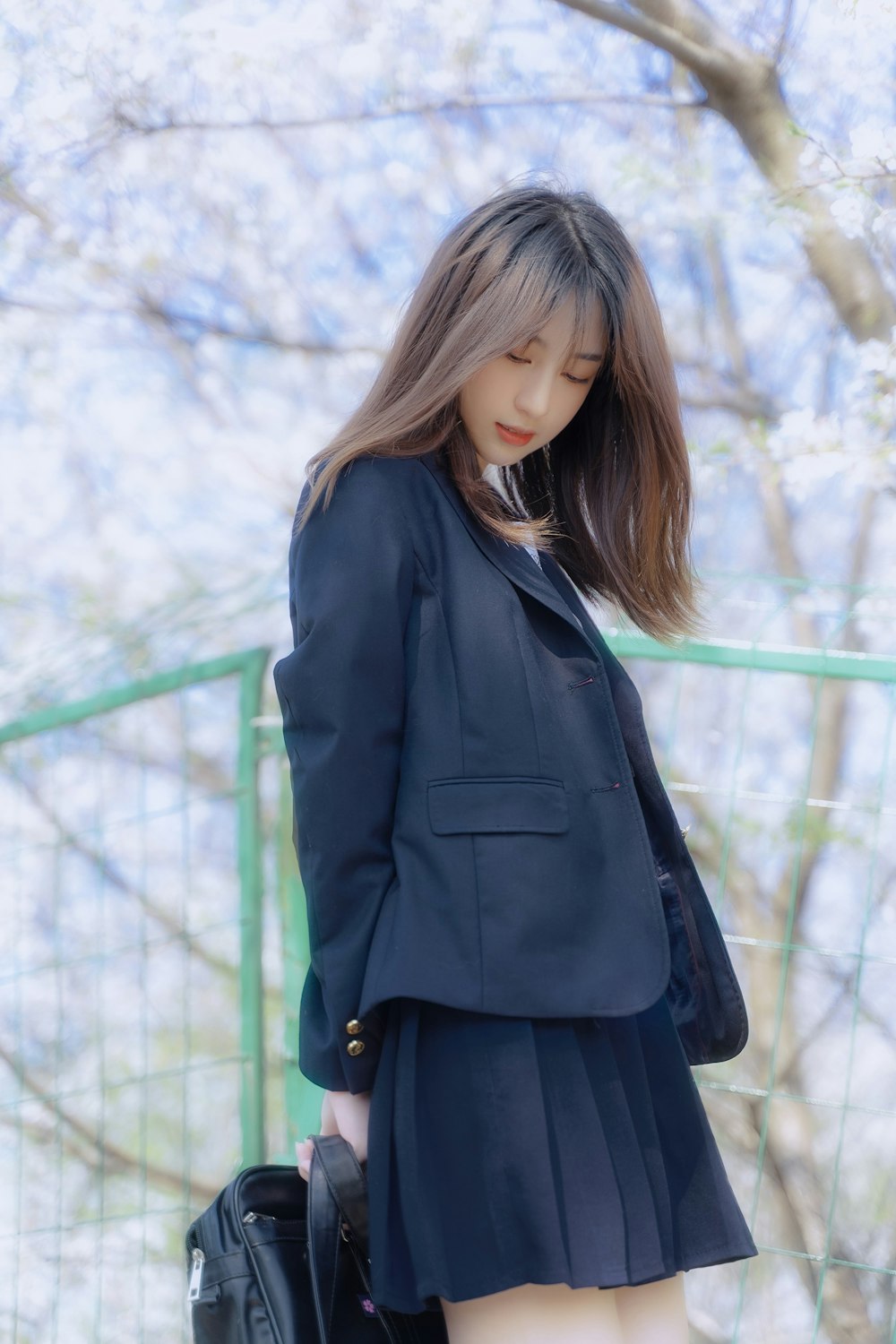 woman in black coat standing near green metal fence during daytime