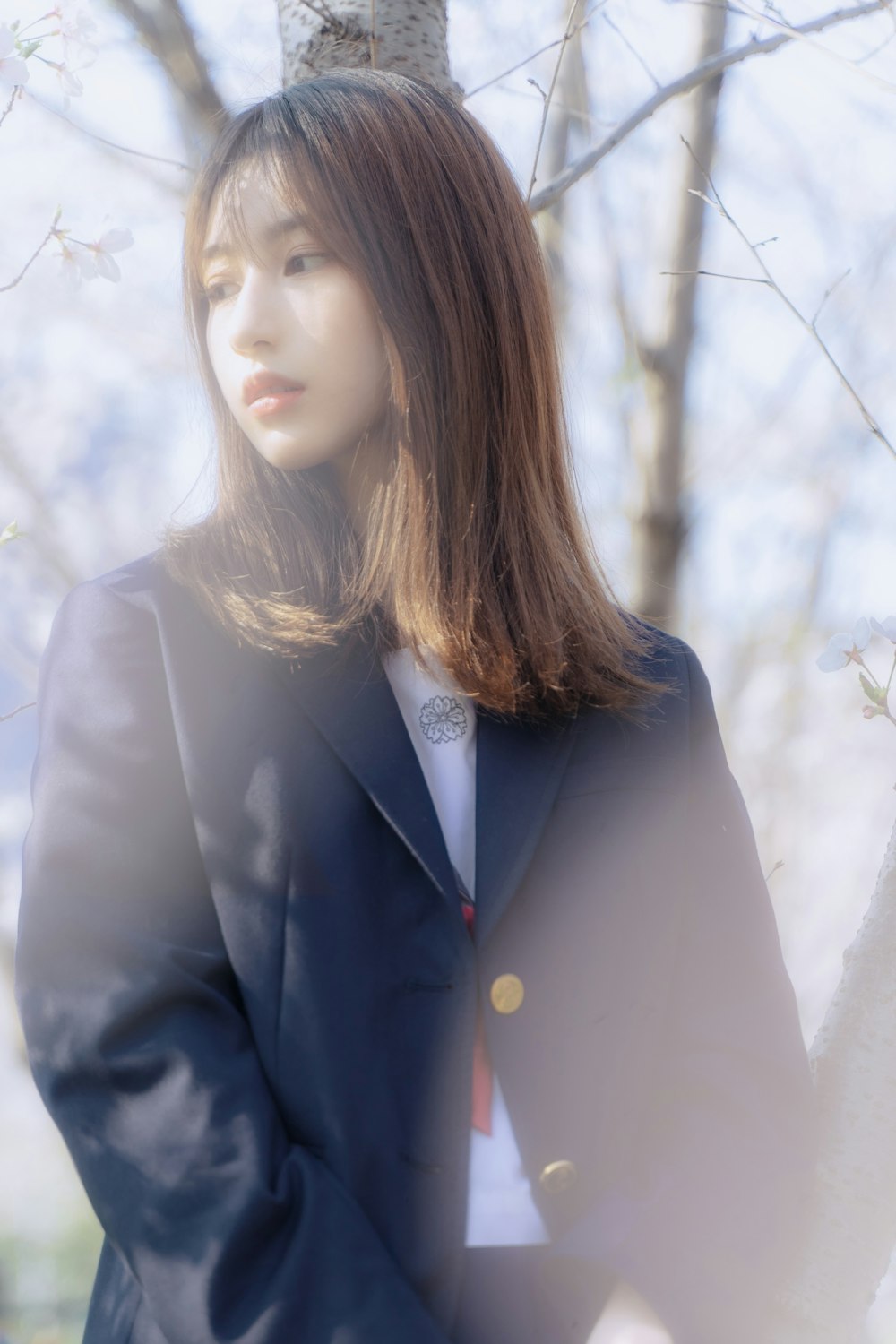woman in blue blazer standing near white leaf trees during daytime