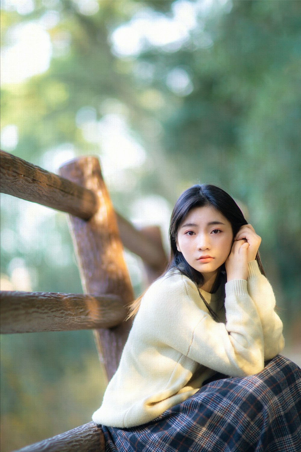 woman in beige long sleeve shirt leaning on brown wooden fence