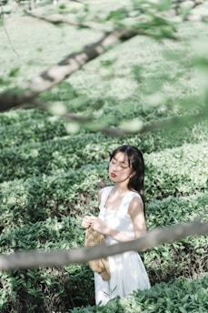 A serene woman meditating outdoors surrounded by soft golden light and army green foliage.