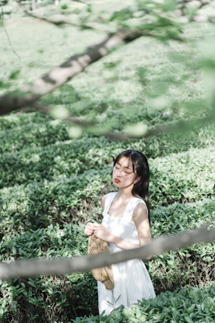 A serene woman meditating outdoors surrounded by lush greenery and golden sunlight.