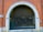 An arched garage entrance with a closed metal security gate. The building is made of red brick with white stone accents around the archway. The area appears to lead to an underground or enclosed space with minimal lighting.