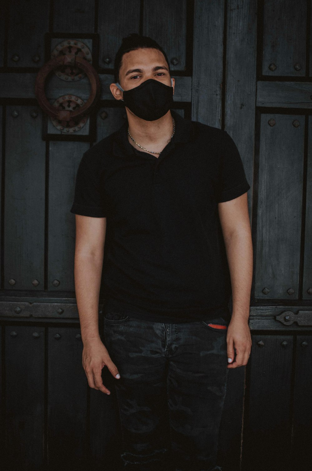 man in black v neck t-shirt and blue denim jeans standing beside black wooden door