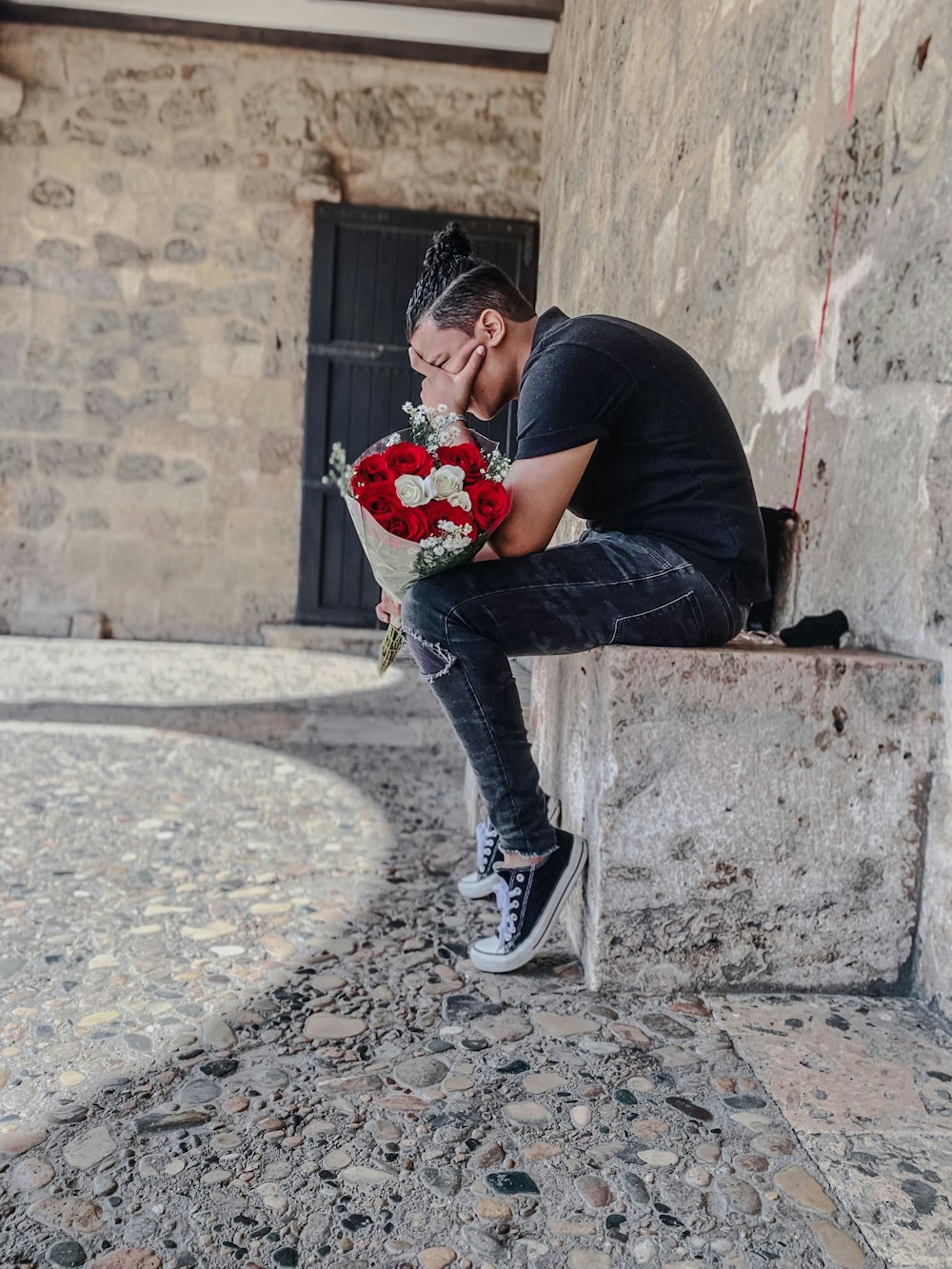 man in black t-shirt and blue denim jeans sitting on concrete wall during daytime