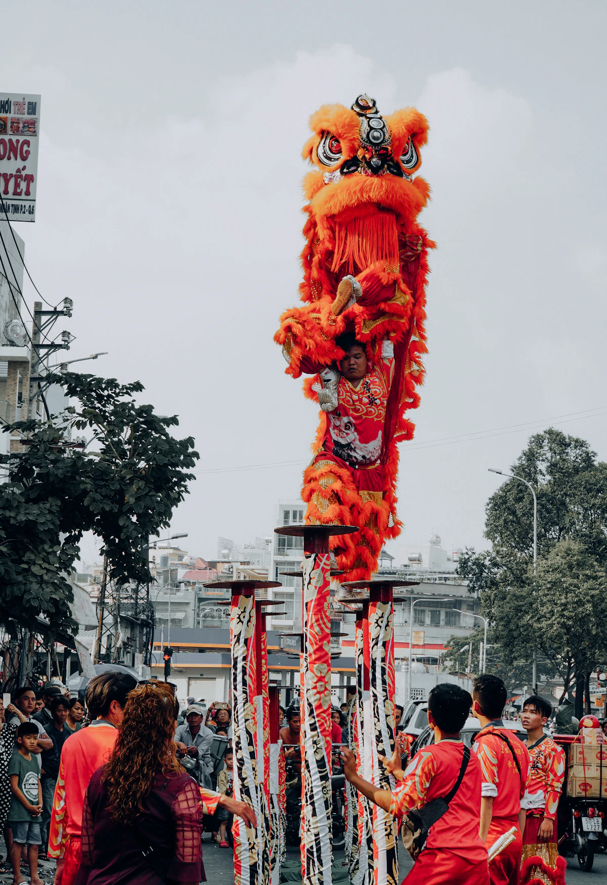 A lion dance performer balancing on the high jong poles against a dramatic sky
