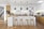 A modern kitchen features a central island with four wooden stools. The cabinetry combines white and natural wood finishes. Black pendant lights hang above the island. The space includes built-in appliances and a large sink. A stairway with a glass railing is visible to the left.