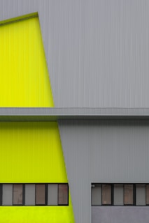 A modern architectural facade featuring a combination of lime green and gray corrugated metal panels. The design includes a series of rectangular windows in a horizontal arrangement, providing a sleek and minimalist aesthetic.