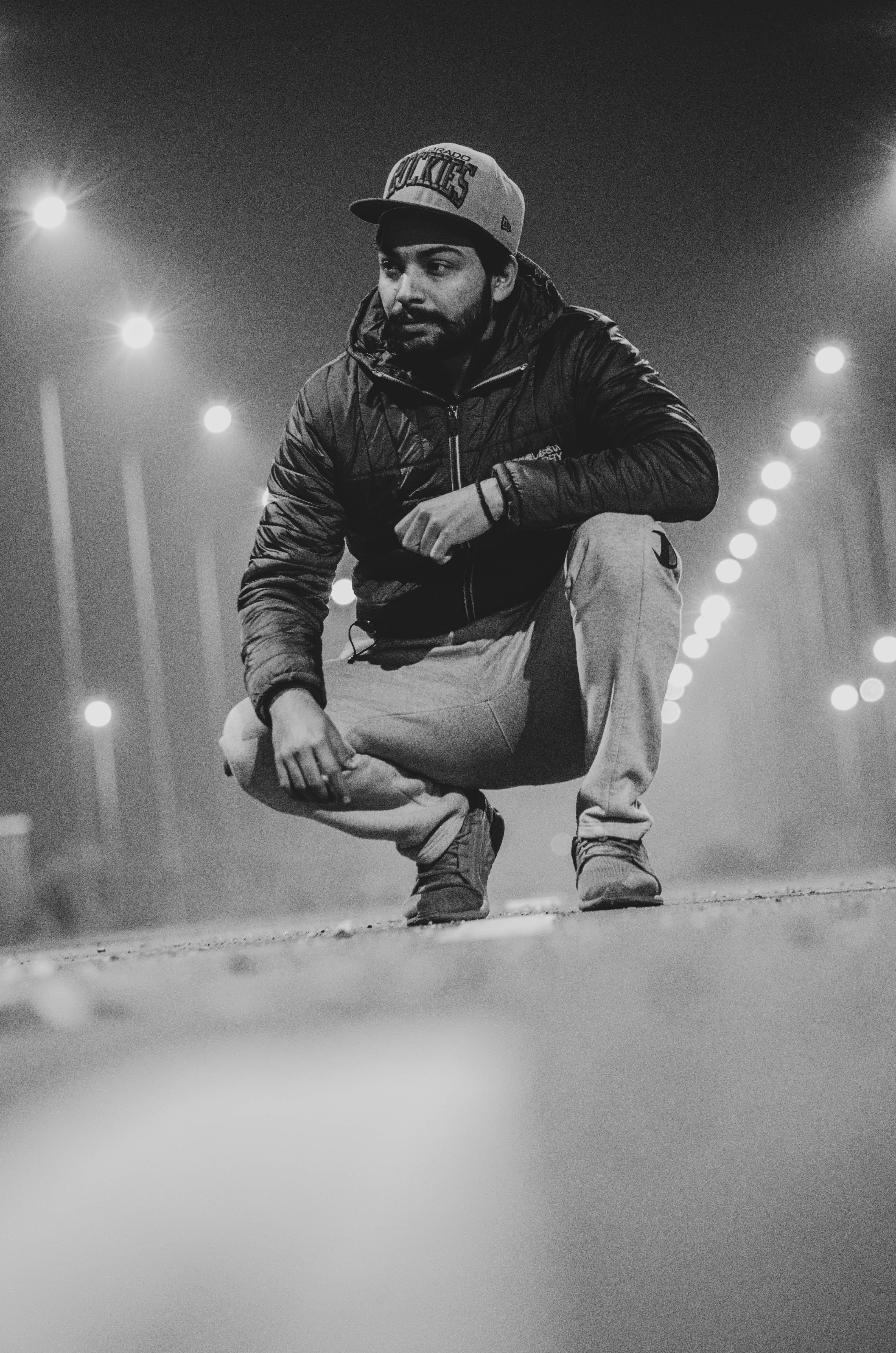 man in black leather jacket and gray denim jeans sitting on concrete pavement