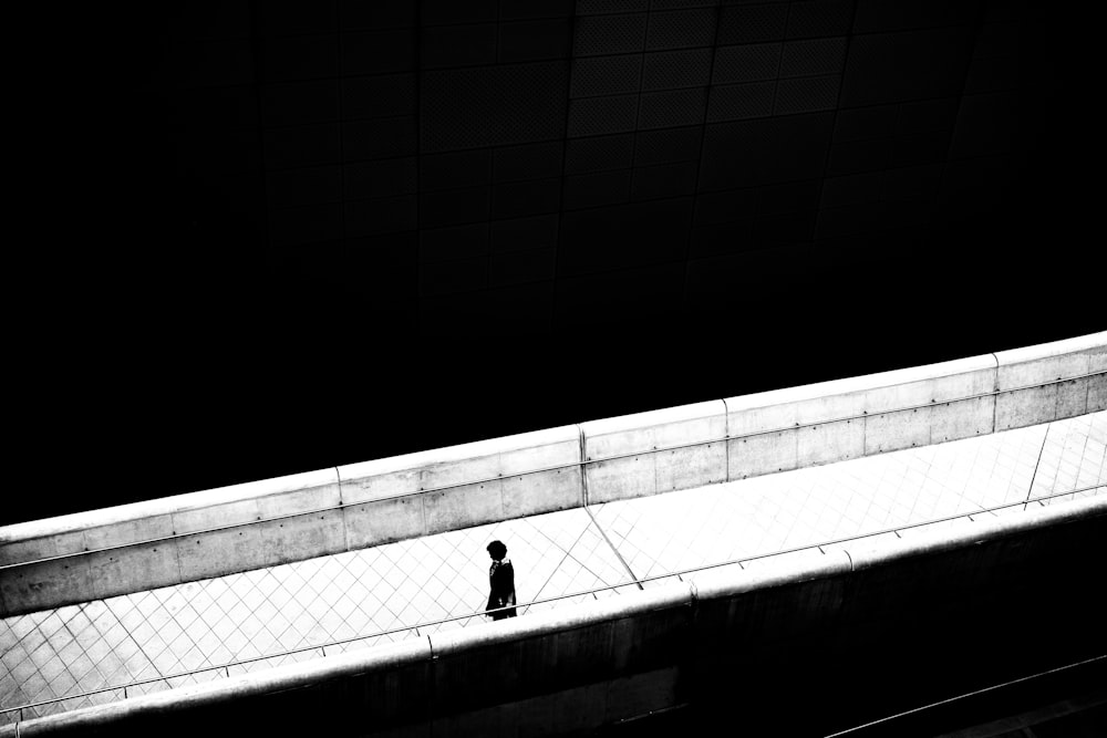 person in black jacket walking on white concrete bridge