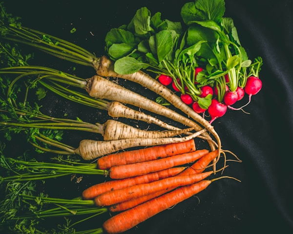 Carrots and green leaves on black surface