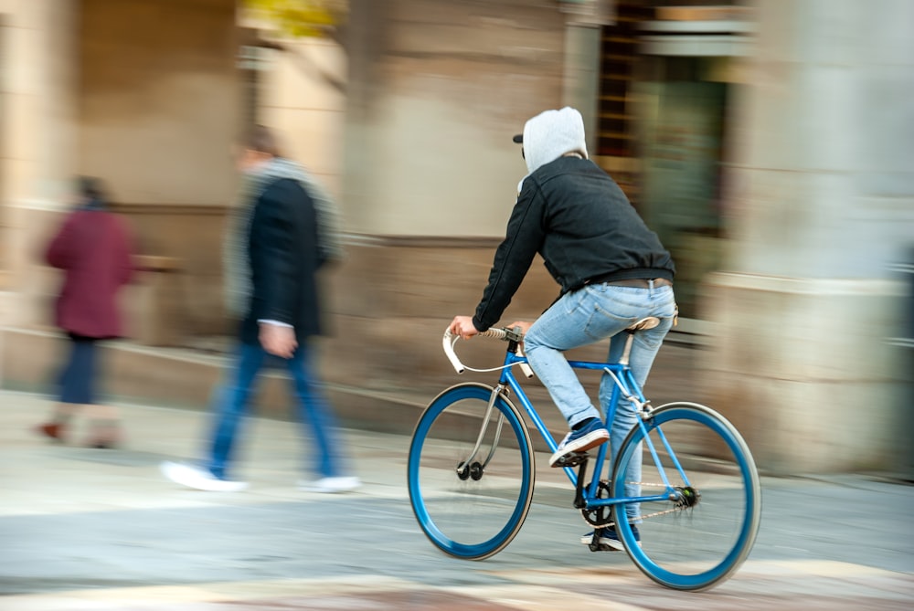 man in black jacket riding blue bicycle on road during daytime