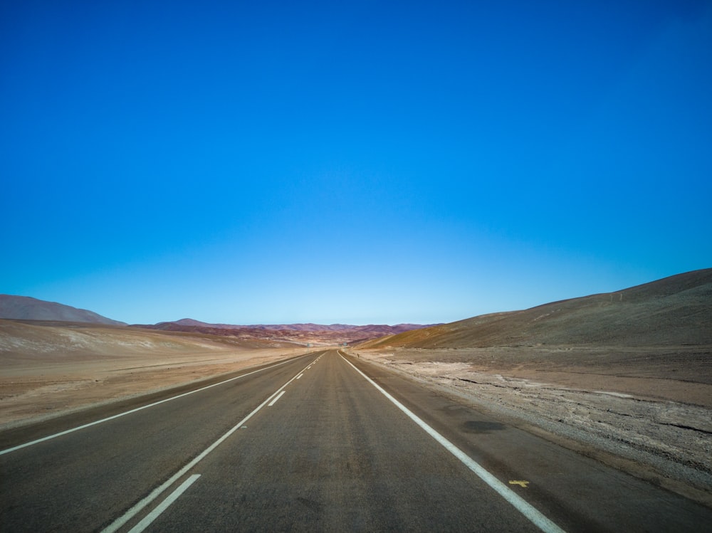 black asphalt road in the middle of brown field under blue sky during daytime