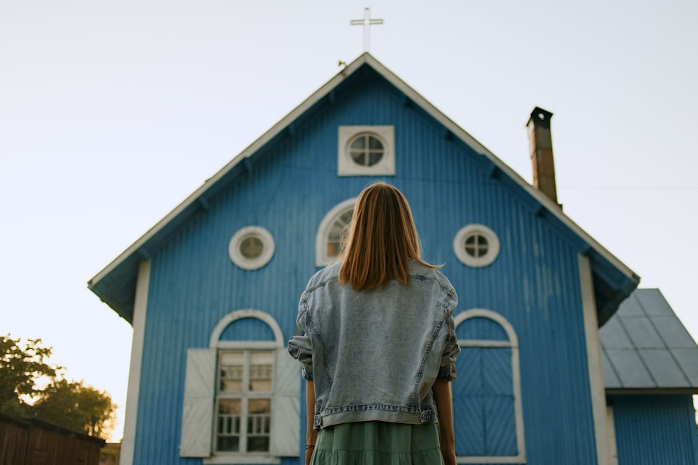 woman in gray shirt standing in front of blue and white wooden house